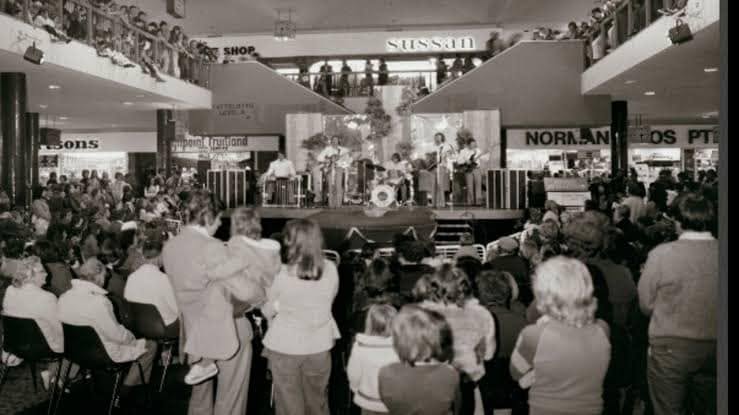 Black and white photo of a live band performing on Centre Stage to a large crowd on two levels, with Sussan and Pet Shop signage visible