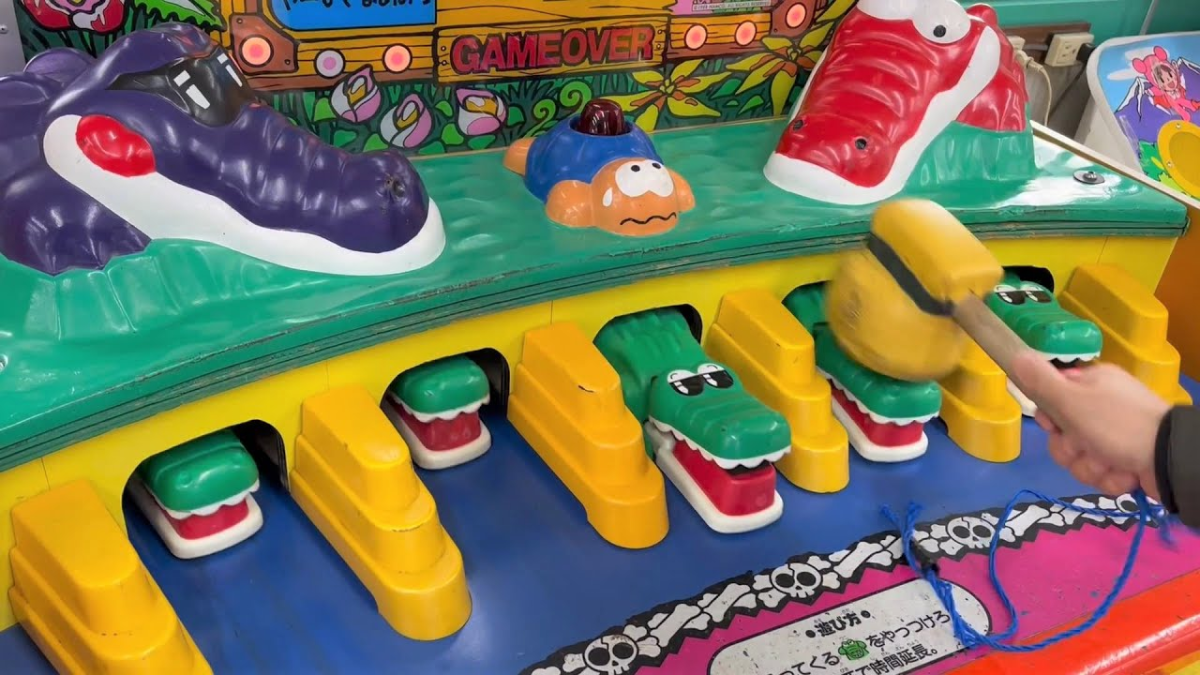 Someone playing the crocodile-whacking arcade game with a mallet, green crocodile heads sliding out sideways from yellow bases