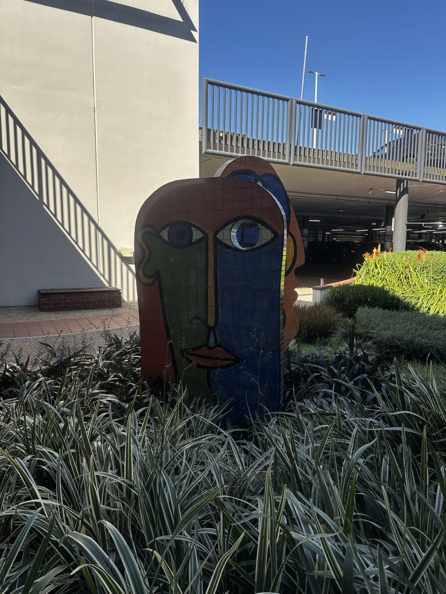 A tiled mosaic face sculpture in blue, green and orange near a car park ramp