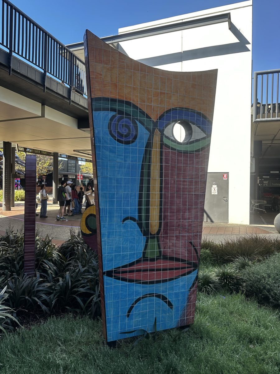 A tall tiled mosaic face sculpture in orange, blue and maroon outside a shopfront