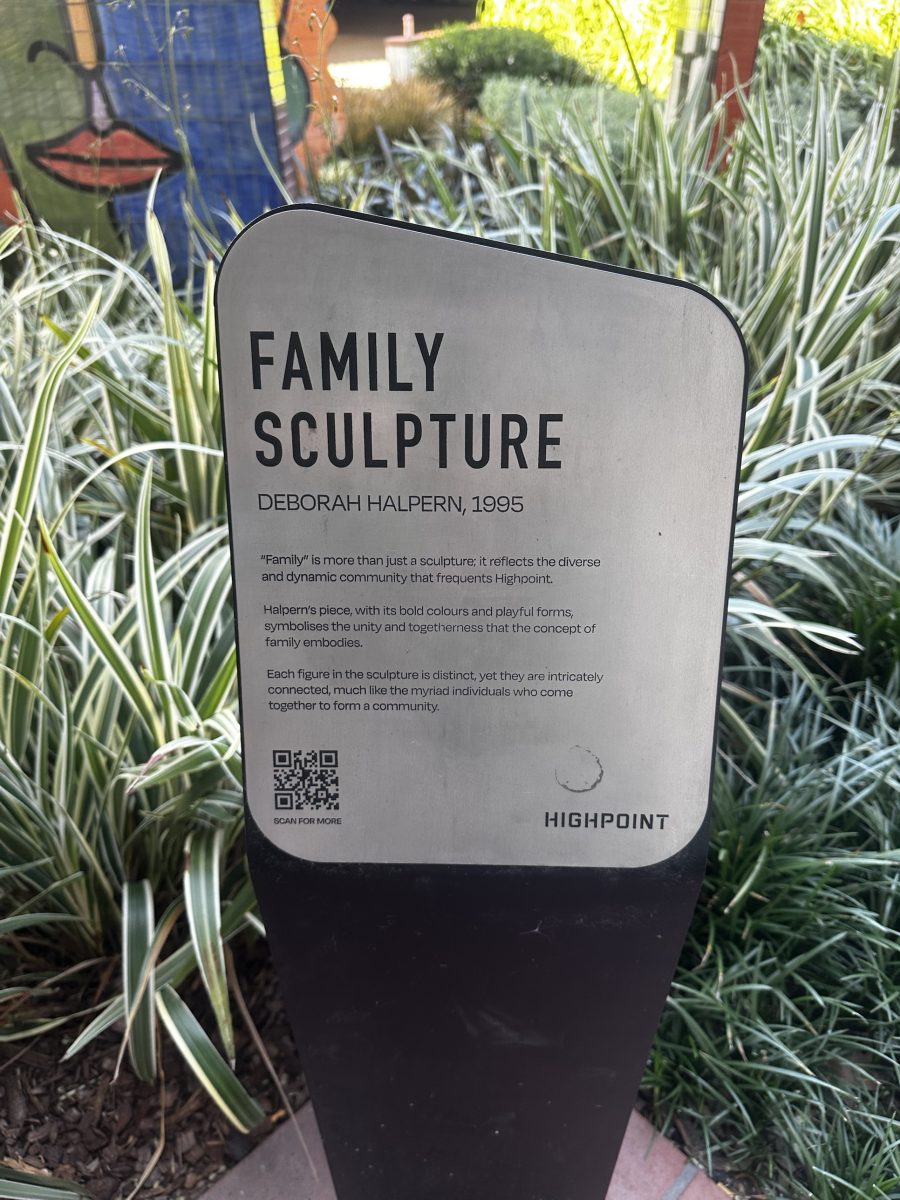 A stainless steel plaque titled "Family Sculpture" by Deborah Halpern, 1995, set among garden plants