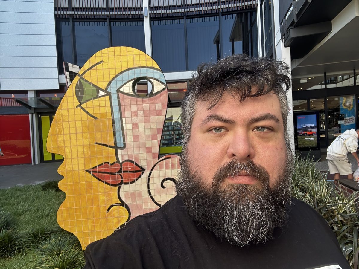 Keith standing in front of the yellow and pink face sculpture from the Family artwork at Highpoint