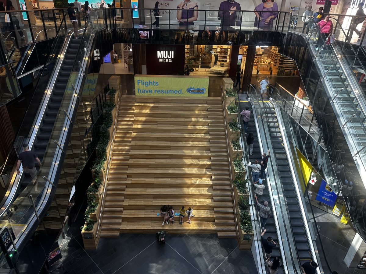 Overhead view of a wide modern timber staircase at Highpoint leading up towards a MUJI store, with escalators either side