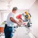 two men cutting wood with a circular saw in a white room