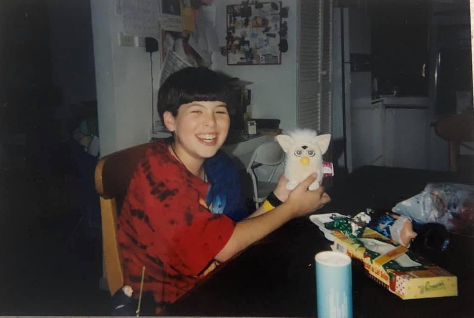 Young Keith grinning and holding his sister's white Furby